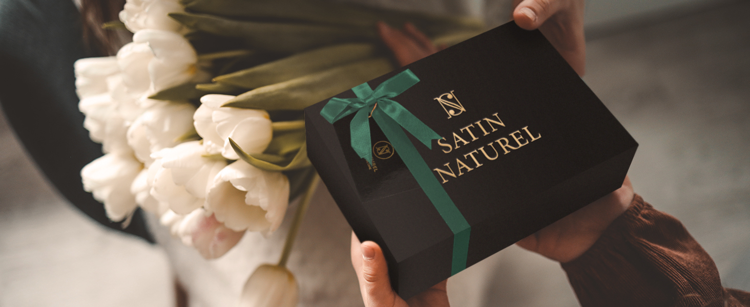 Coffret cadeau vert foncé avec texte doré, photographié aux côtés de fleurs blanches dans des conditions de faible éclairage.