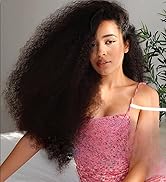 Portrait sur fond neutre avec des plantes d'intérieur, avec de longs cheveux bouclés volumineux et un haut texturé rose à fines bretelles