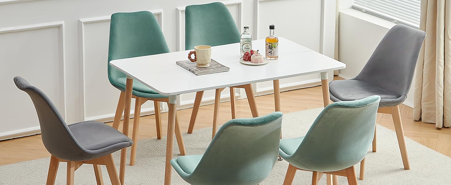 avec table rectangulaire blanche et six chaises. Quatre chaises bleu sarcelle et deux chaises grises avec pieds en bois dans une pièce lumineuse.