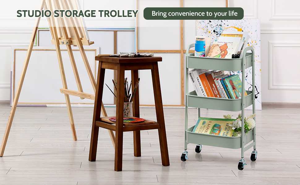 Chariot roulant vert menthe à trois niveaux avec livres et fournitures artistiques. Un tabouret en bois et un chevalet se trouvent à proximité. Le texte indique « Studio Storage Trolley » et « Facilitez votre vie ».