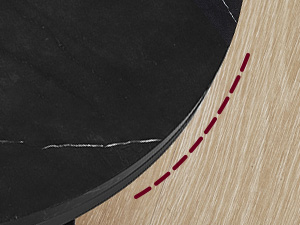 Gros plan d'un bord incurvé où un matériau noir rencontre du bois clair, avec une ligne pointillée rouge indiquant une couture ou une