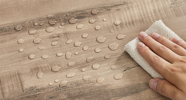 Des gouttelettes d'eau perlent sur une surface en bois traité, la surface étant essuyée à la main avec un chiffon blanc, démontrant