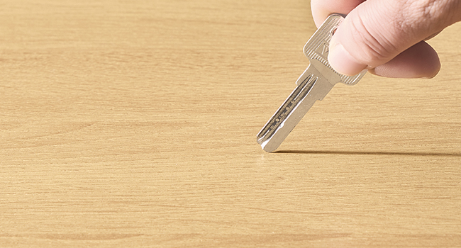 Une main tenant une clé en métal au-dessus d'une surface en bois clair. La clé possède un bord dentelé et est positionnée comme si elle était sur le point d'être insérée dans une serrure