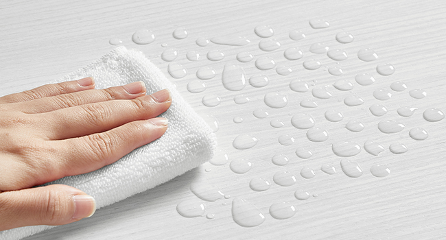 Gros plan de gouttelettes d'eau sur la surface d'un tissu ou d'un matériau imperméable blanc, avec la main démontrant ses propriétés hydrofuges