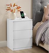 Table de chevet blanche à trois tiroirs, affichant un smartphone en train de charger sur le dessus. Vase avec feuilles d'automne et vue partielle de la literie grise visible.