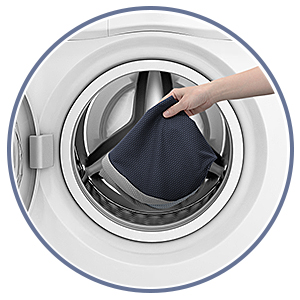 Vue aérienne de l'intérieur du tambour de la machine à laver avec la main plaçant un article en tissu foncé à l'intérieur du tambour en acier inoxydable.