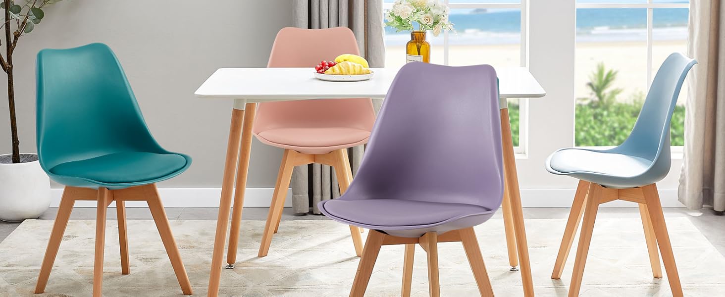 avec table ronde blanche et quatre chaises de différentes couleurs (bleu sarcelle, violet, bleu) avec pieds en bois, près d'une fenêtre avec vue sur l'océan