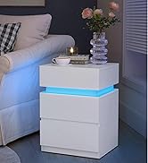 Table de chevet blanche avec éclairage LED bleu entre les tiroirs. Comprend trois tiroirs et contient un vase avec des fleurs roses, des livres et une tasse à café.