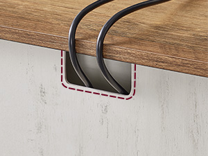 Deux clips de gestion des câbles noirs incurvés fixés sous le bord d'un bureau ou d'une étagère en bois, avec support adhésif visible.