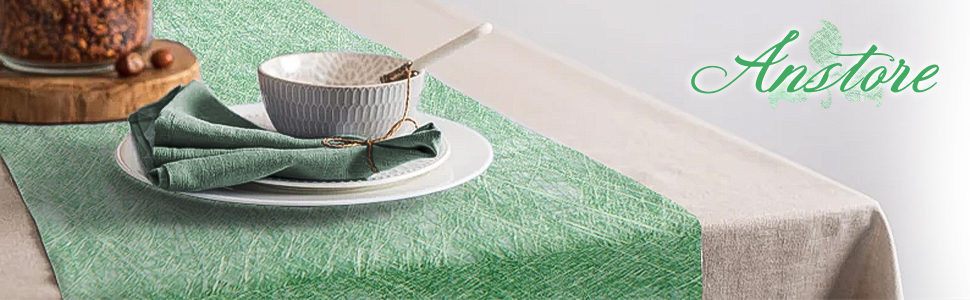 Set de table avec assiettes blanches, serviette verte et vue partielle d'un dessert sur une nappe verte et blanche. Le texte « Anstore » est visible.