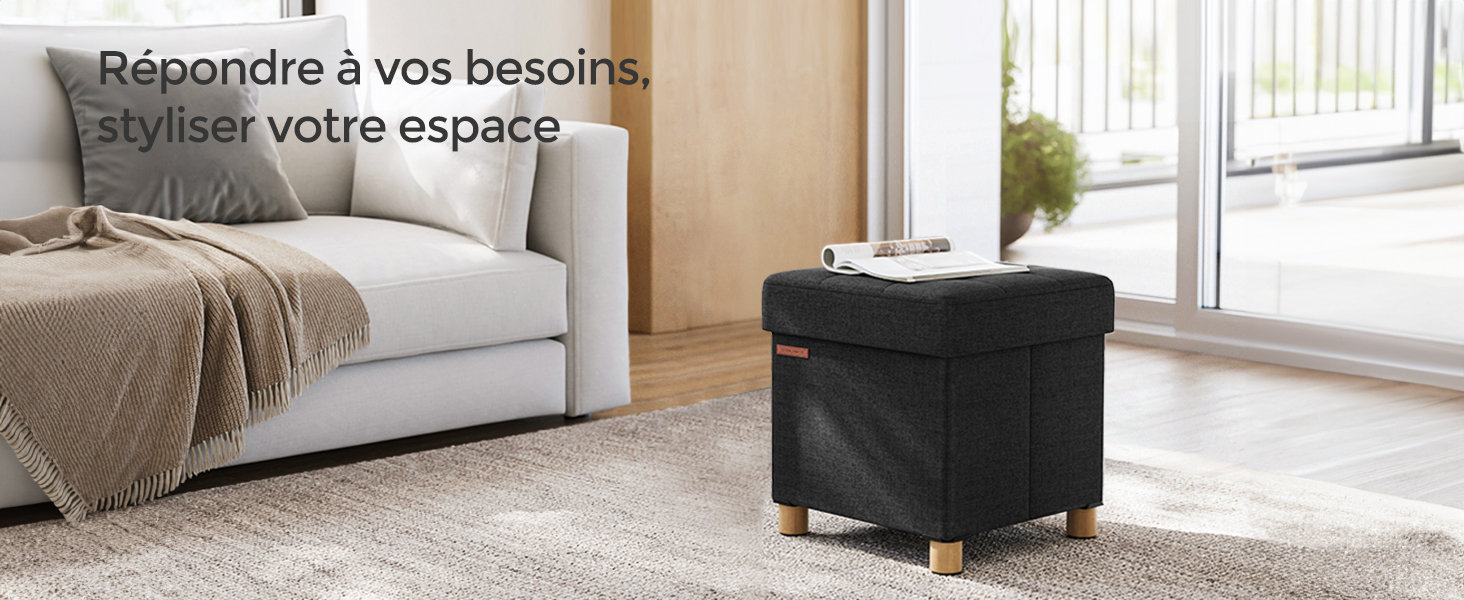 Salon moderne doté d'un pouf de rangement noir avec pieds en bois, placé près d'un canapé gris clair et de grandes fenêtres.