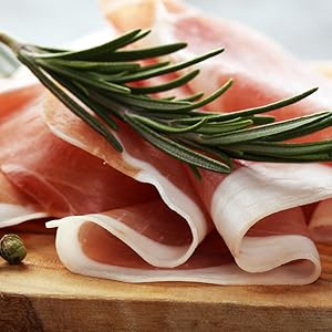 Plans rapprochés de tranches fines de prosciutto ou de jambon disposés sur une surface en bois avec des brins de romarin frais en guise de garniture.