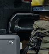 Vue partielle d'un appareil gris étiqueté « CFX » au premier plan, avec un sac à dos beige et un équipement noir en arrière-plan. L'intérieur du véhicule est visible.