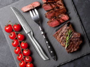 Tranches de bifteck grillées sur une ardoise foncée à la fourchette, accompagnées d'une grappe de tomates cerises sur la vigne.