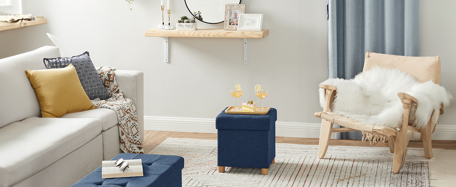 Salon moderne doté d'un pouf et d'un cube de rangement bleu marine, d'un canapé beige clair, d'une chaise en bois avec couvre-lit en fourrure et d'une étagère murale