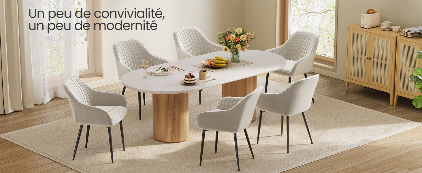 avec table ronde blanche, base en bois et six chaises de couleur claire. Buffet et décor visibles en arrière-plan.