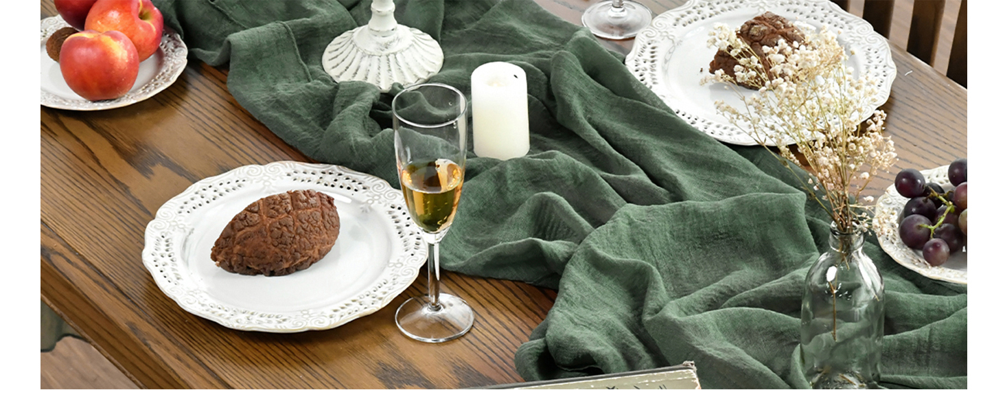 Set de table avec des assiettes blanches, un drap vert, un verre à vin et divers produits alimentaires, dont des pommes et un plat rond blanc.