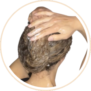 Les mains appliquent du shampoing ou du produit capillaire sur les cheveux courts et mouillés. L'image circulaire montre un mouvement de mousse à l'arrière de la tête.