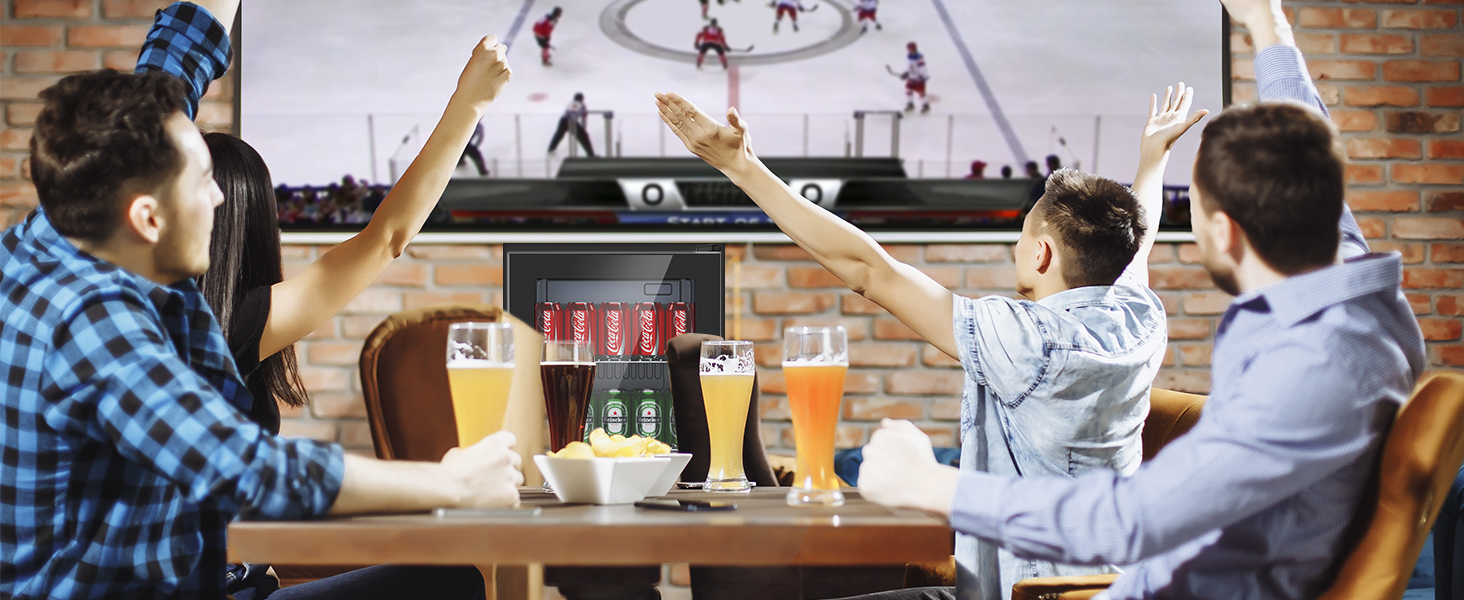 Trois hommes regardent le sport à la télévision dans un bar, levant les bras en signe de fête. Différents verres à bière sur la table.