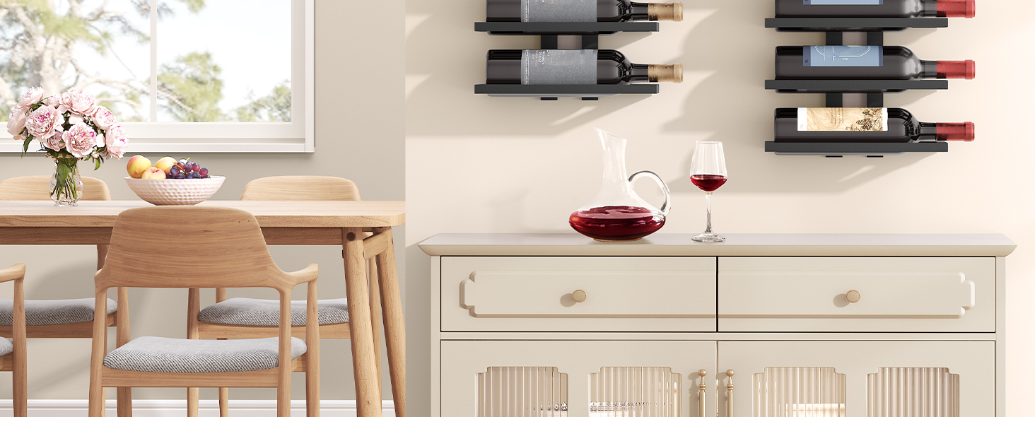 Intérieur de cuisine avec table en bois, chaises et armoires blanches. Verres à vin et bouteille visibles sur le comptoir. Étagères murales en arrière-plan.