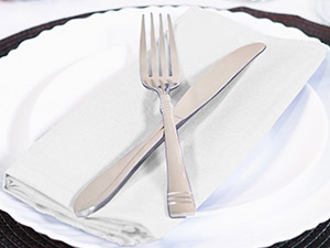 Fourchette et couteau en argent posés sur une assiette blanche avec une serviette blanche, posés sur une surface sombre