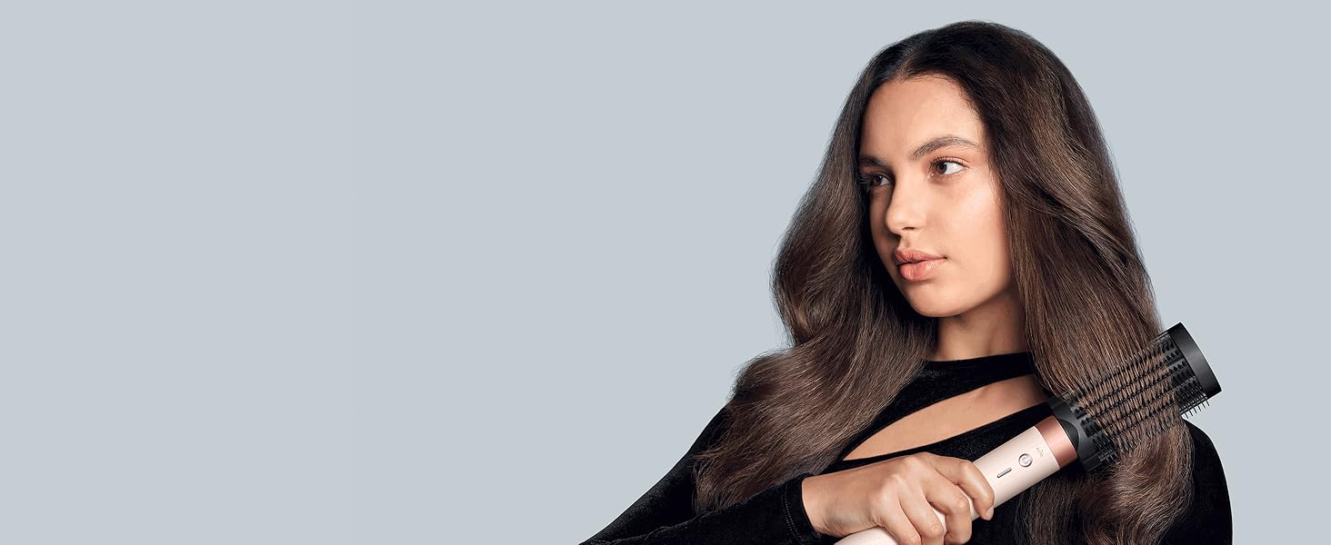 Photo de studio professionnelle montrant de longs cheveux ondulés foncés coiffés avec divers produits coiffants sur fond gris.