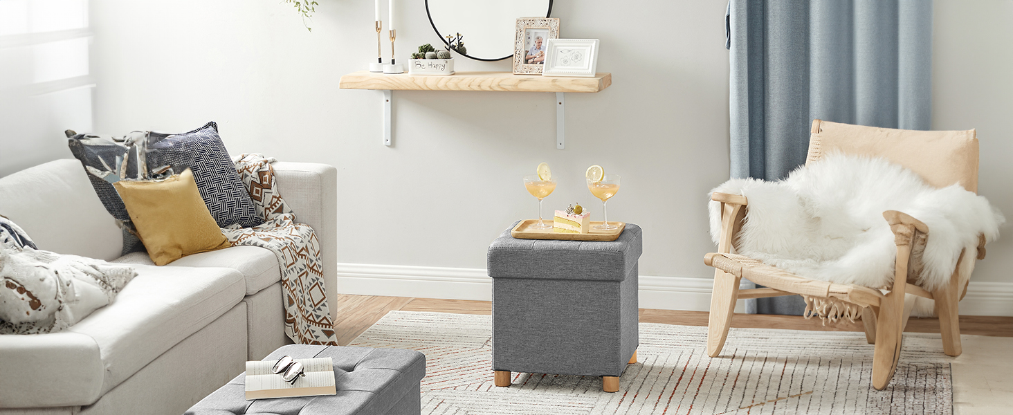 Salon moderne avec canapé gris, coussins à motifs, pouf gris, chaise blanche avec couvre-lit en fourrure et étagère flottante sur des murs bleu pâle