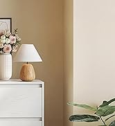 avec base en bois et abat-jour blanc sur commode blanche. Arrangement floral dans un vase à proximité. Murs beiges et vue partielle de la plante.