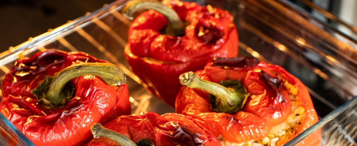 Poivrons rouges rôtis sur une grille, carbonisés et légèrement frisés, avec des marques visibles sur le gril et un aspect juteux