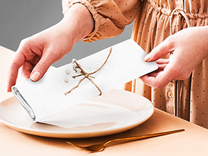 Les mains utilisent des ciseaux dorés pour couper une ficelle blanche attachée autour d'une plaque blanche sur une surface en bois. Concept de vaisselle et de découpage à cordes