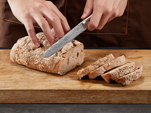 Trancher à la main une miche ronde de pain croustillant sur une planche à découper en bois, avec plusieurs tranches déjà coupées