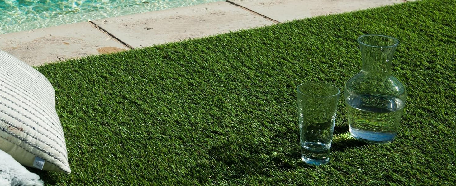 Scène extérieure montrant des récipients en verre disposés sur une surface de pelouse verte à proximité d'un élément architectural blanc. Verrerie transparente qui capte la lumière du soleil.