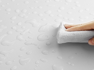 Gros plan d'une main essuyant une surface texturée avec un chiffon blanc. Démontre une action de nettoyage ou de séchage sur un fond à motifs de couleur claire