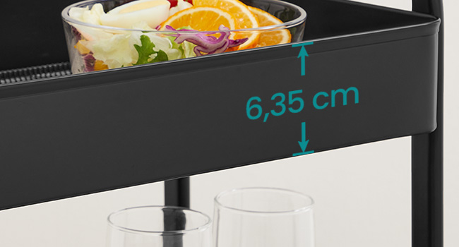 Chariot de service noir avec un bol en verre de salade mixte. Mesure de 6,35 cm indiquée pour la profondeur du chariot. Deux verres vides visibles en dessous.