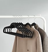 Tringle de placard blanche minimaliste avec plusieurs cintres en velours noir retenant des manteaux beiges et gris contre un mur gris clair