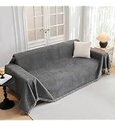 Housse de canapé ou couverture texturée grise présentée sur le canapé, avec des bords décoratifs à pompons et une construction en tissu léger