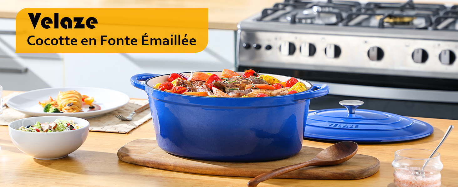 Cocotte en fonte émaillée bleue avec couvercle sur planche de bois. Rempli d'un plat coloré, éventuellement d'une cocotte ou d'un ragoût. La cuisinière est visible en arrière-plan.