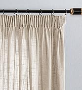 Tringle à rideau noire avec embout doré supportant un rideau plissé beige. La tige possède plusieurs anneaux pour la suspendre. Le tissu du rideau semble texturé et semi-transparent