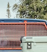 Grande glacière isotherme avec couvercle vert dans la caisse du camion, derrière une barrière de chargement en fil métallique orange. Arbres visibles en arrière-plan.