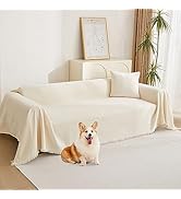 Housse de canapé de couleur crème sur canapé dans le salon. Chien Corgi assis sur le sol devant. La chambre dispose de plantes, d'œuvres d'art encadrées et de rideaux.