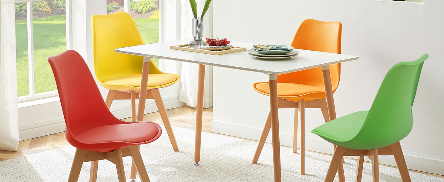 avec table en bois clair et quatre chaises colorées en rouge, jaune, orange et vert, situé dans une pièce lumineuse avec une grande fenêtre.